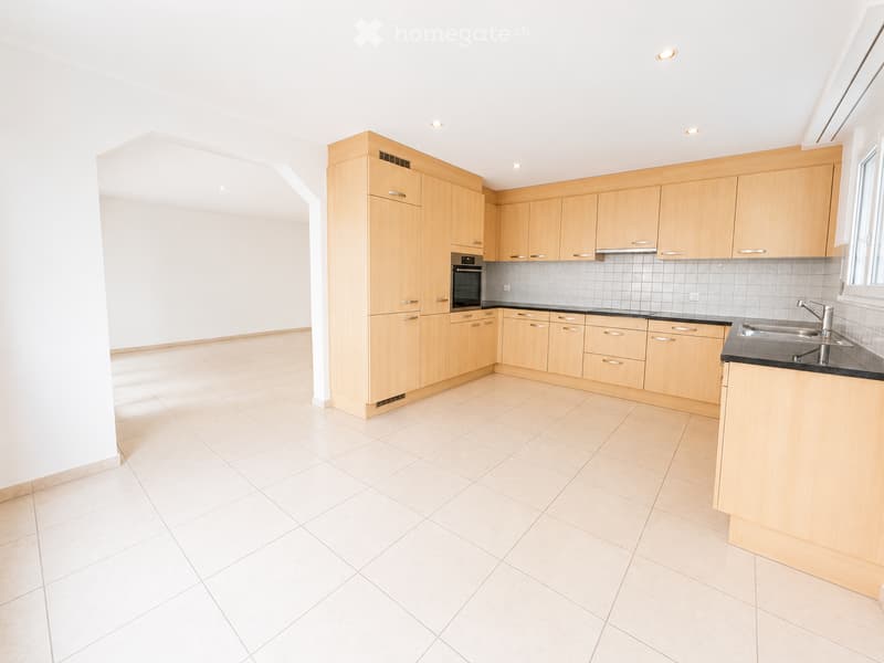 Empty kitchen with light wooden cabinets, tiled floor, and a sink, no appliances or furniture present.