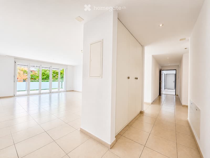 Empty hallway with white walls, tiled floors, and large sliding glass doors leading to an outdoor area.