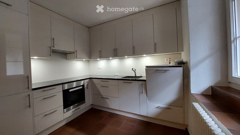 Modern kitchen with light grey cabinets, stainless steel appliances, and a black countertop.