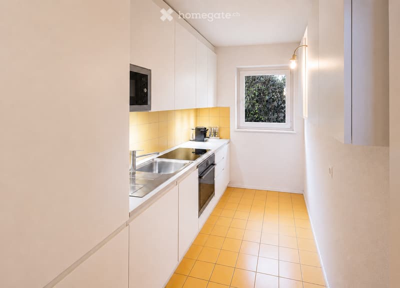 Modern kitchen with white cabinets, stainless steel sink, oven, microwave, and coffee maker. Yellow tiled backsplash and floor.