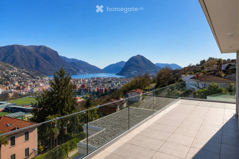 Balcony with modern glass railing, tiled floor, overlooking a scenic lake and mountain view.