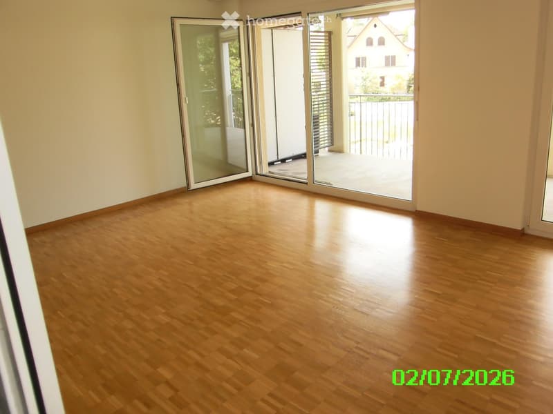 Empty room with wooden flooring and large sliding glass doors leading to a balcony.