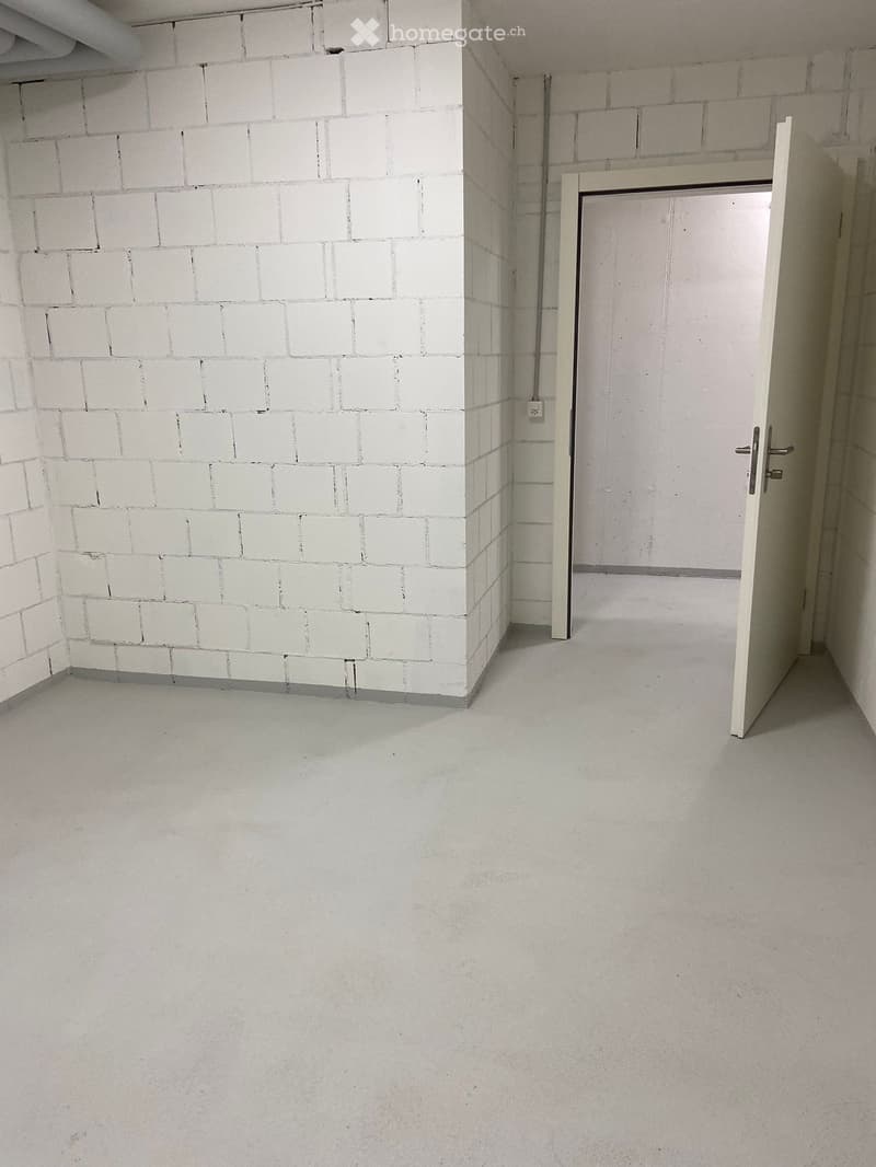 Empty room with white brick walls, concrete floor, and a single open door leading to another space.