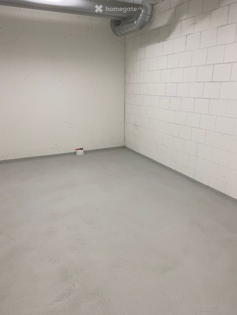 Empty room with concrete floor and white tiled wall, featuring a metal pipe and a small sign on the floor.