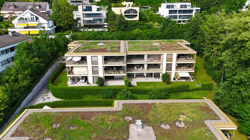 Aerial view of a modern residential complex with multiple buildings, green roofs, balconies, and surrounding greenery.