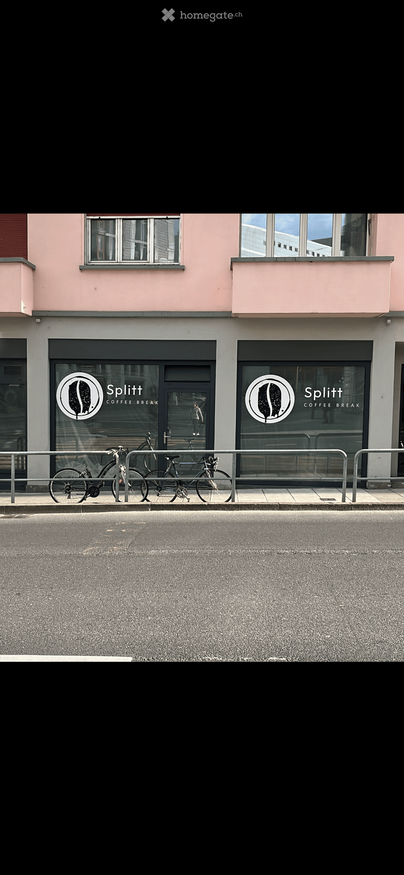 Pink building with two windows and two signages on front entrance, bicycles parked on metal railings in front.