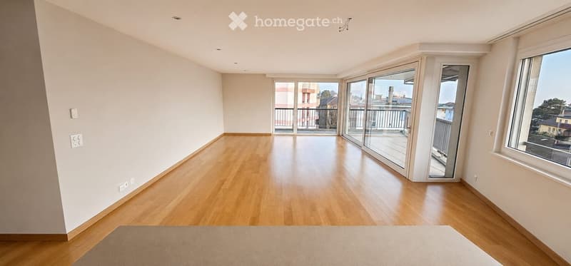 Empty room with wooden flooring, large windows, and sliding glass doors leading to a balcony.