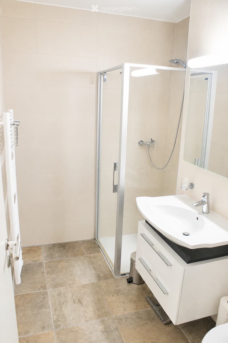 Modern bathroom with beige tiles, a white sink with a chrome faucet, a mirrored cabinet, a glass-enclosed shower, and a towel on a rack.