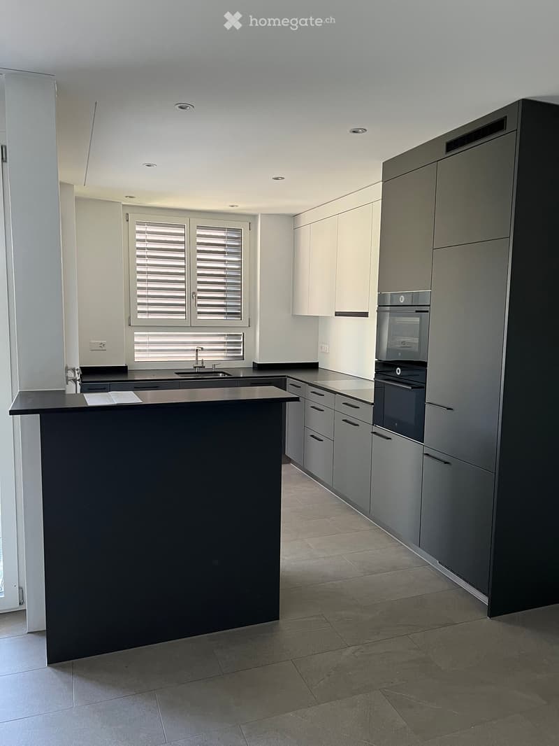 Modern kitchen with grey cabinets, black countertop, built-in oven, and a central island with sink and faucet.
