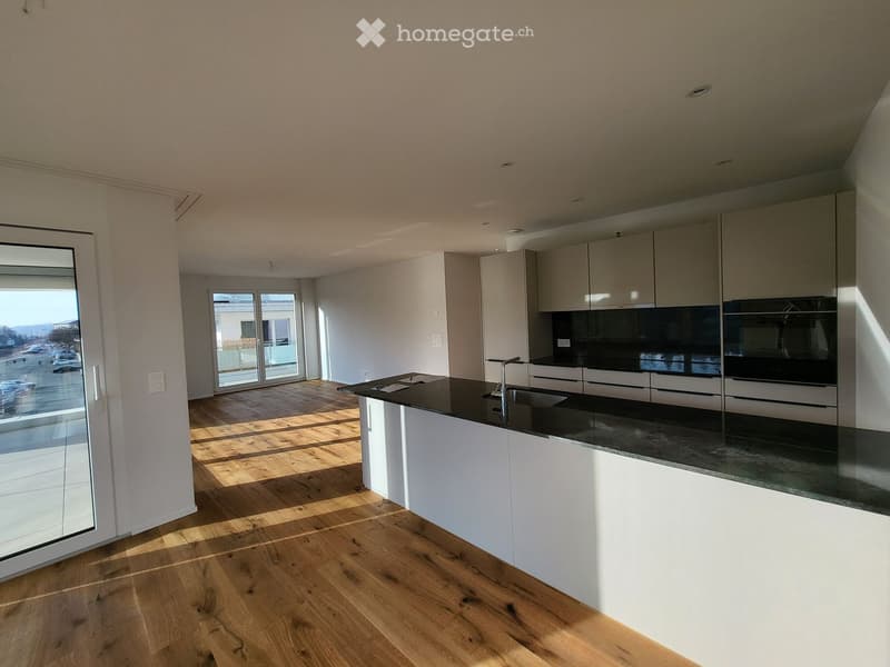 Modern kitchen with light-colored cabinets, a black countertop, and a wooden floor. Features a kitchen island with a sink and faucet, and built-in appliances including an oven.