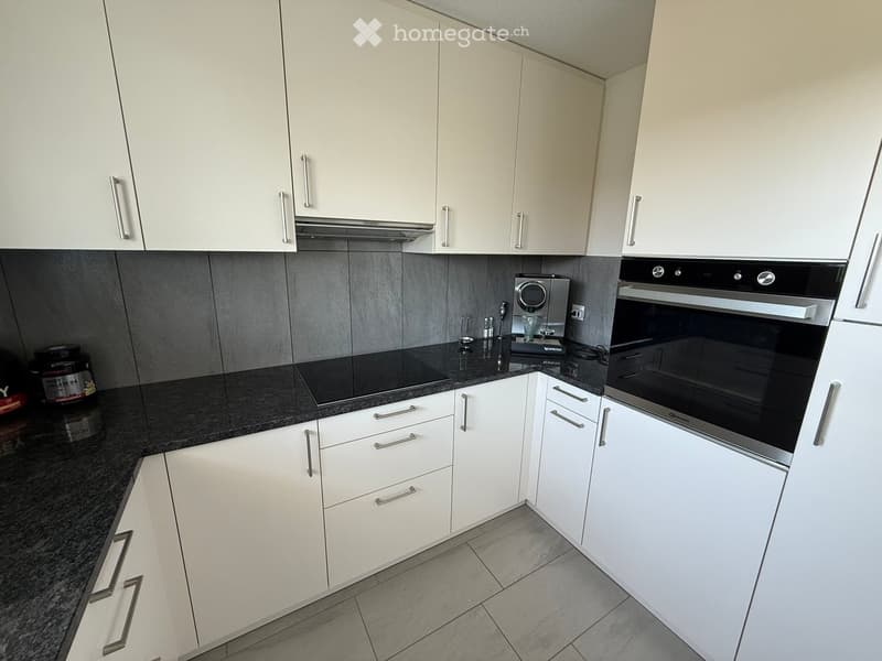 Modern kitchen with white cabinets, black countertops, and stainless steel appliances including an oven and microwave.