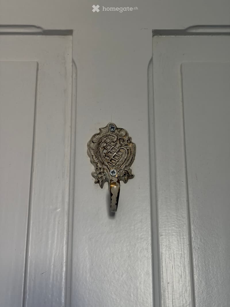 Close-up of a decorative door handle with a heart-shaped design and intricate carvings, mounted on a white door frame.