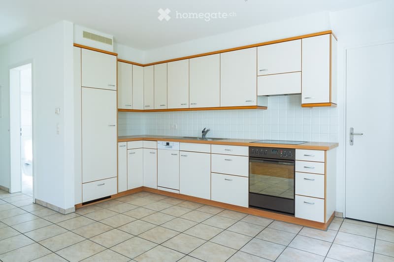 Modern kitchen with white cabinets, wooden trim, tiled floor, and built-in appliances including a sink, oven, and dishwasher.