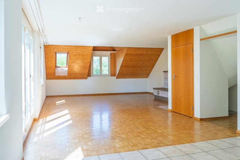 Empty room with wooden flooring, white walls, and large windows allowing natural light. The ceiling features wooden beams and skylights.