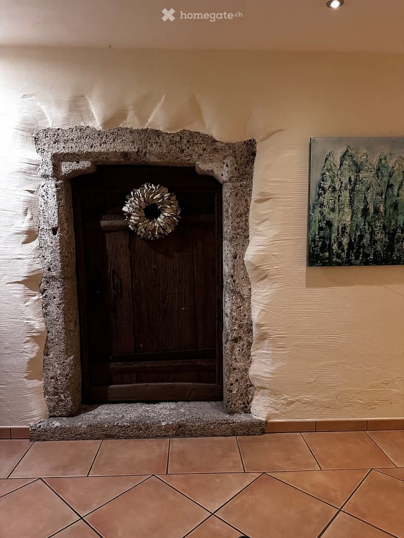 A rustic fireplace with a wooden door, a decorative wreath, and a painting on the wall.