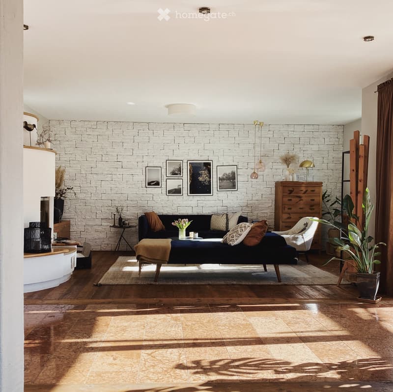 Living room with a dark blue sofa, coffee table, wooden floor, white brick accent wall, and decorative items including a plant and picture frames.