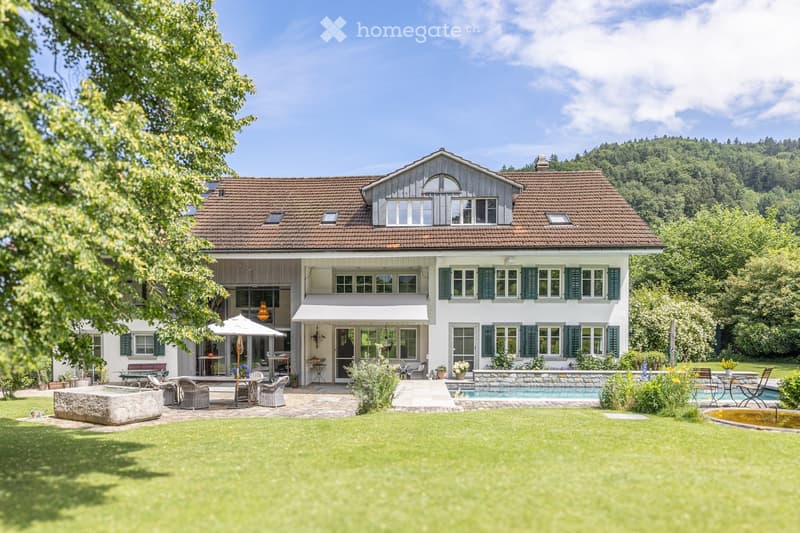 Two-story house with a tiled roof, white walls, green shutters, and a spacious garden with a swimming pool, outdoor seating, and a patio area.
