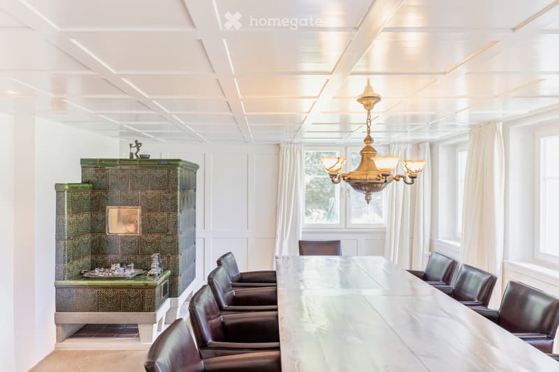 Elegant room with a long wooden table surrounded by leather chairs, a decorative fireplace, and a chandelier hanging from the ceiling.