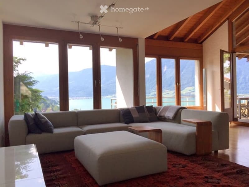 Bright living room with large windows offering a scenic mountain view, featuring a grey sectional sofa, ottoman, coffee table, and floor lamp.