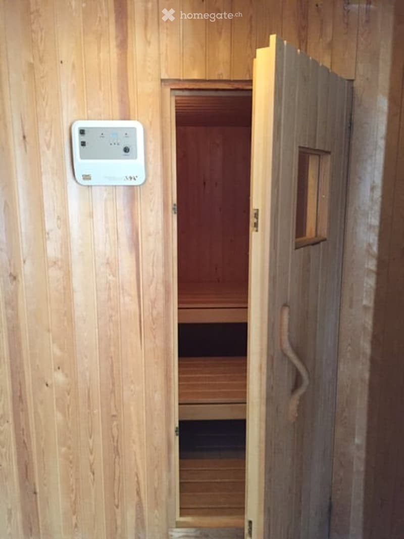 Wooden sauna with a control panel on the wall and an open door revealing the interior bench.