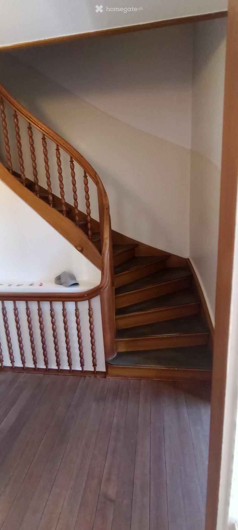 Wooden staircase with a handrail and balusters, leading upwards, with a small grey hat placed on the landing.