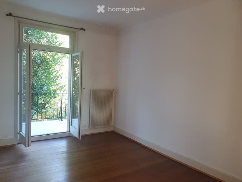 Empty room with wooden flooring, white walls, radiator, and large sliding glass door leading to a balcony.