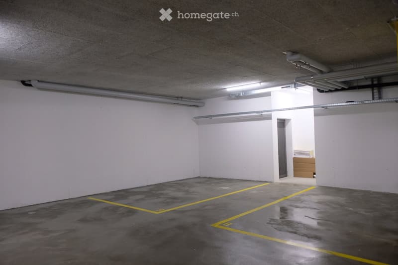 Empty underground parking space with concrete floors, white walls, fluorescent lighting, and yellow parking lines.