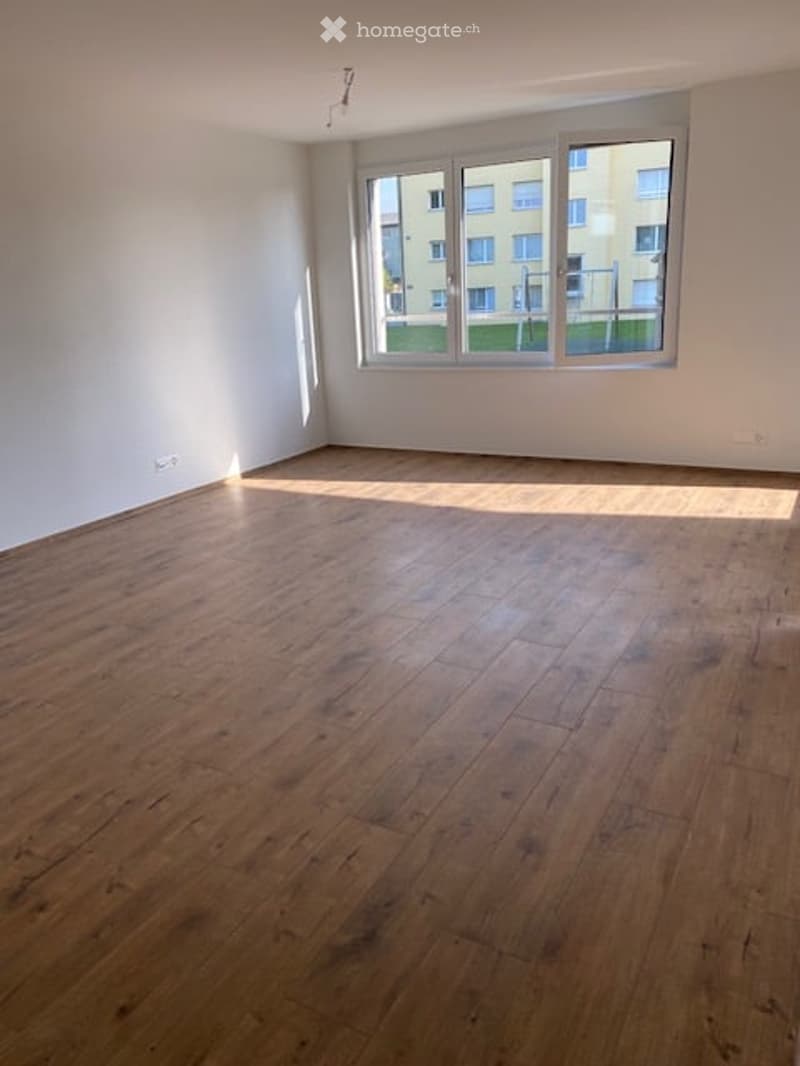 Completely empty room with wooden flooring and large windows, allowing natural light to fill the space.