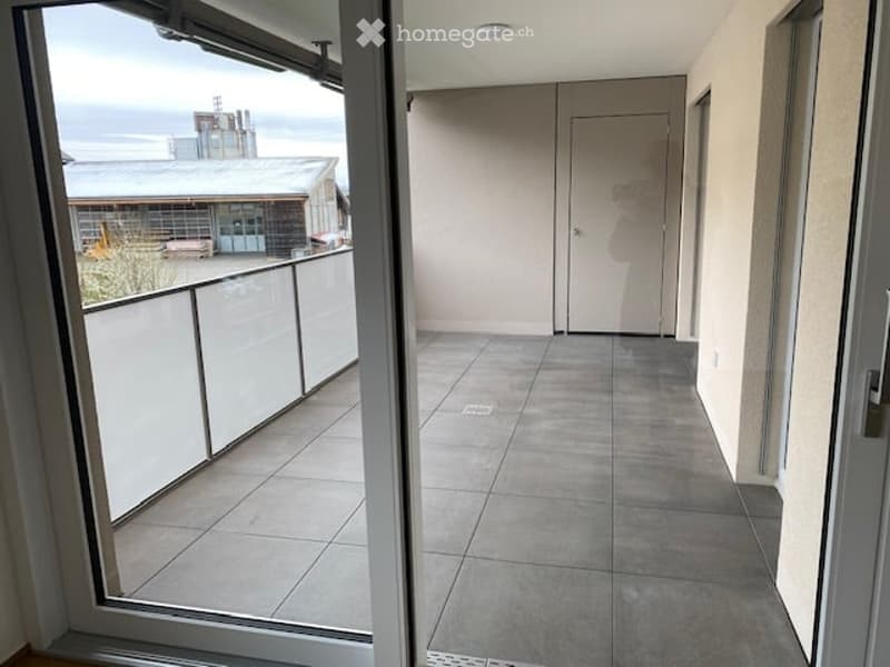 Balcony with tiled floor, white railing, and a view of the ocean and industrial structures.