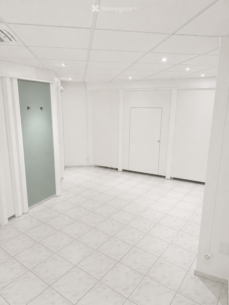 Empty room with white tiled floor and walls, featuring a glass door and white ceiling with recessed lighting.