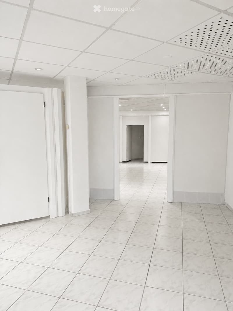 Empty hallway with white walls, tiled floor, and white ceiling with recessed lighting. No furniture or equipment present.