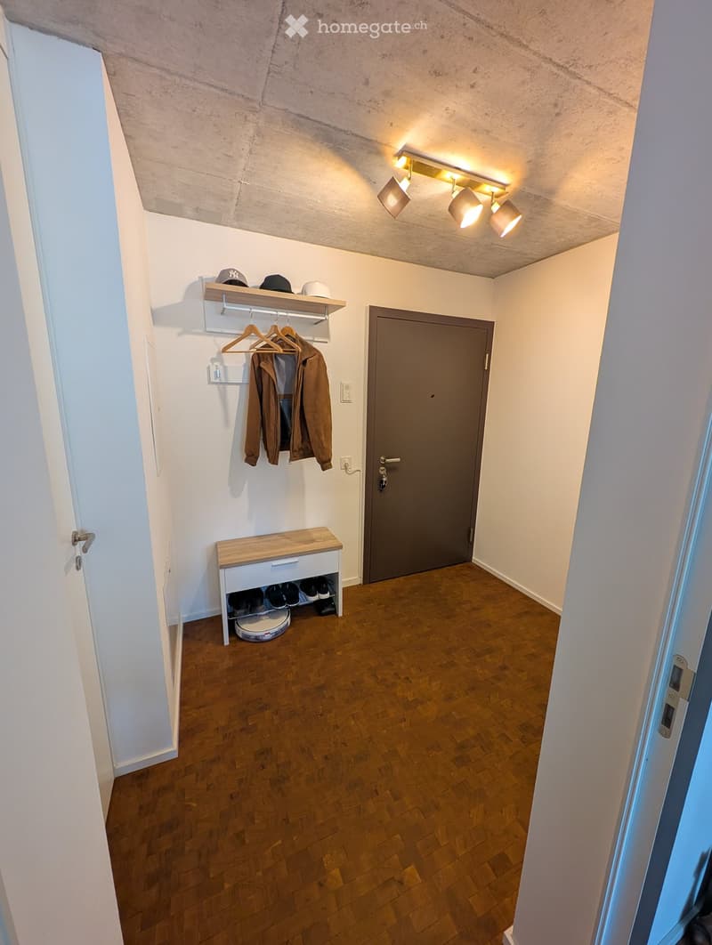 Hallway with wooden flooring, coat rack with jackets, shoe bench, and storage shelf with hats.