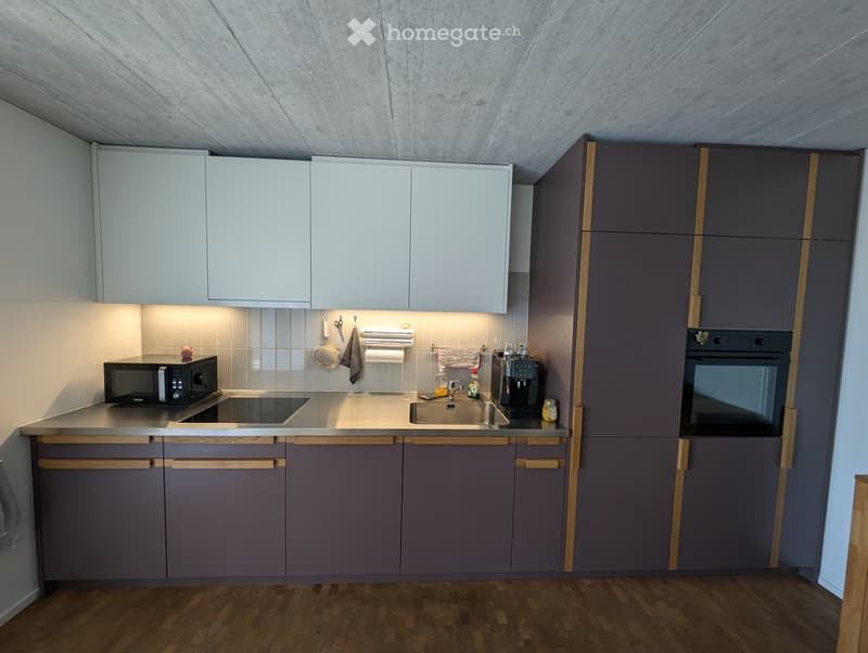 Modern kitchen with grey cabinets, white upper cabinets, stainless steel appliances, and wooden flooring.