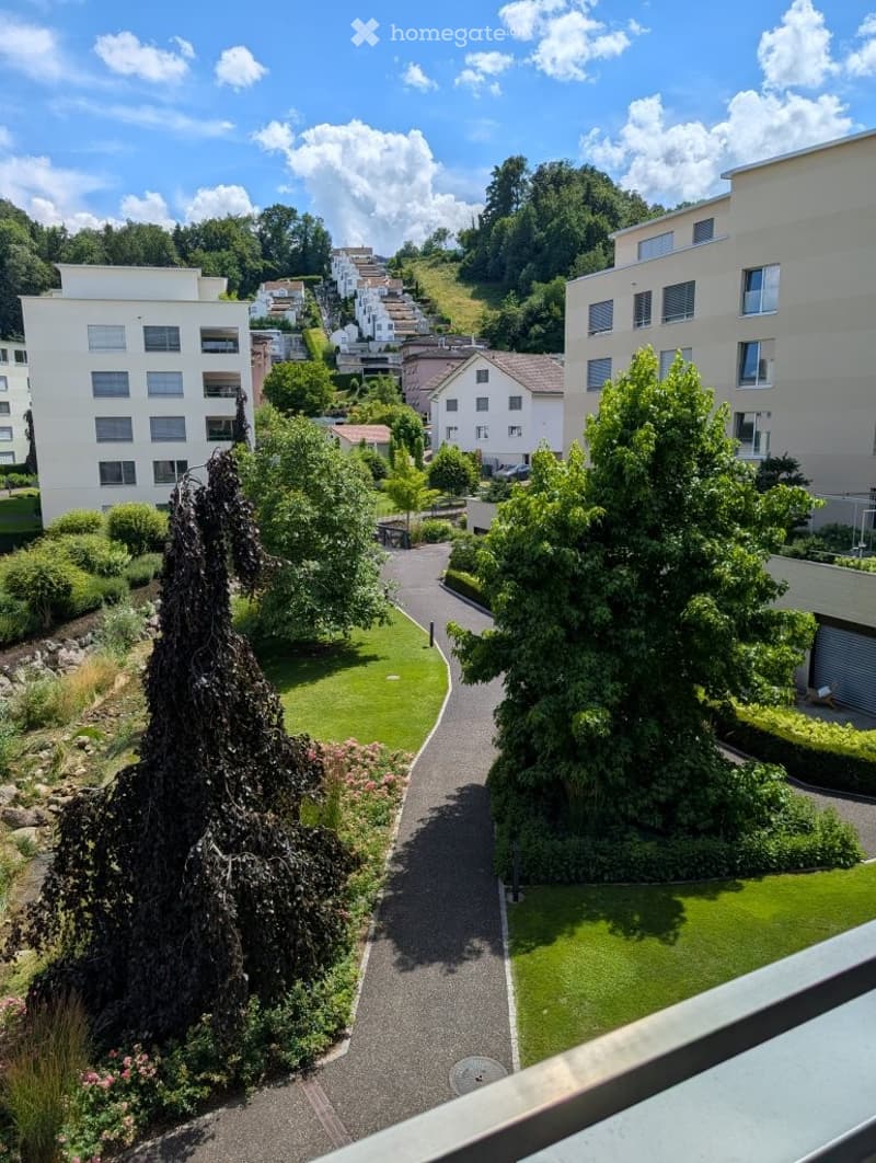 Balcony view of a landscaped garden area with pathways, greenery, and surrounding residential buildings.