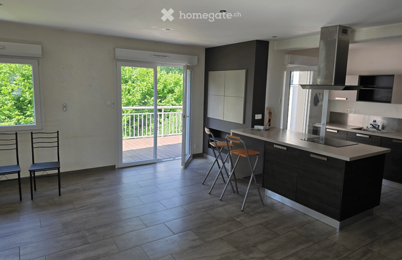 Modern kitchen with dark cabinets, a central island, and a balcony access through large sliding doors. Two chairs and two stools are placed near the island.