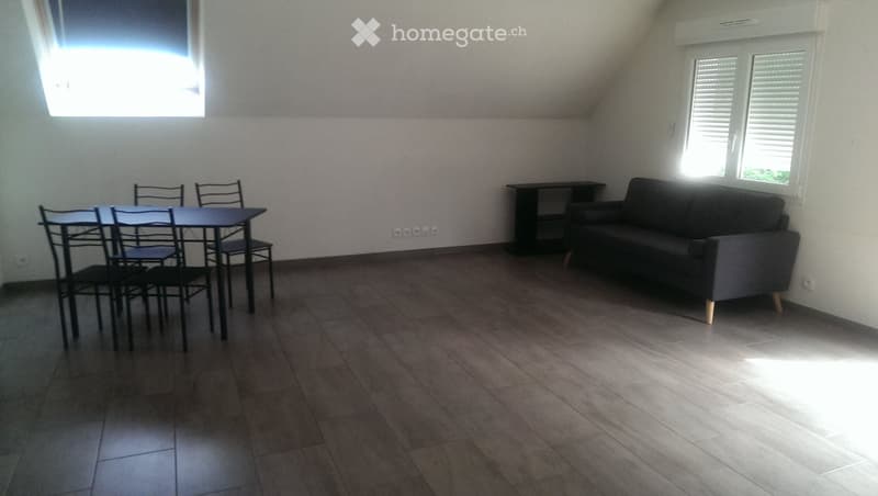 A furnished room with a sofa, dining table, and chairs, featuring wooden flooring and large windows.