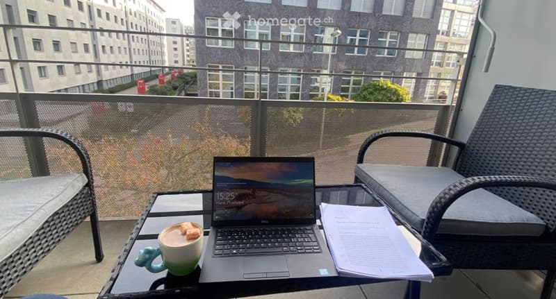 Balcony with wicker chairs, glass table, laptop, coffee mug, and papers.