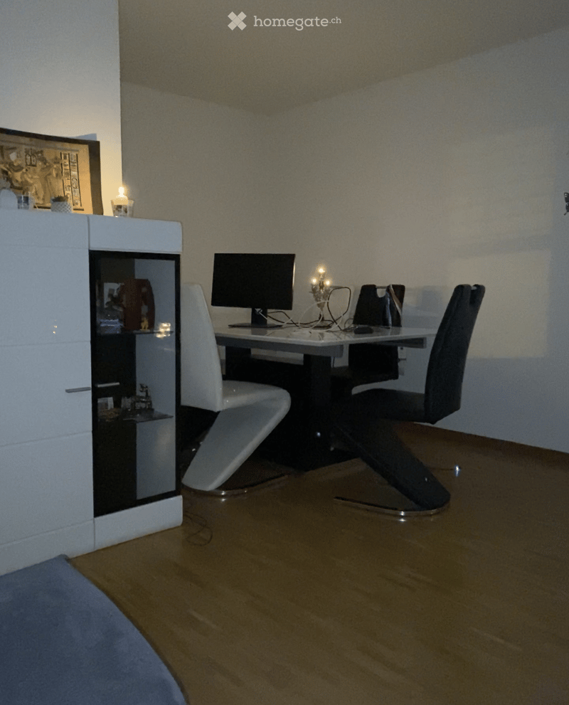 A modern office or study room with a wooden floor, a white cabinet, a desk with a computer screen, and two chairs.