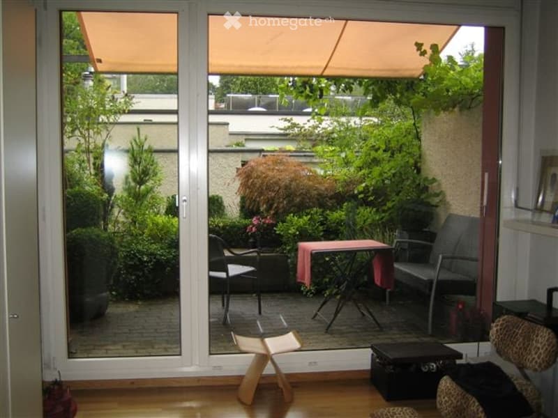 Balcony with outdoor furniture including a table, chairs, and a small bench, surrounded by greenery and plants.