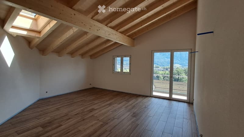 Empty room with wooden flooring, exposed wooden beams on the ceiling, large skylight, and sliding glass door leading to a balcony.