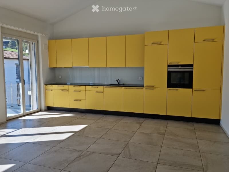 Bright kitchen with yellow cabinets, tiled floor, and a sink. The space is well-lit with natural light coming through a large window or door.
