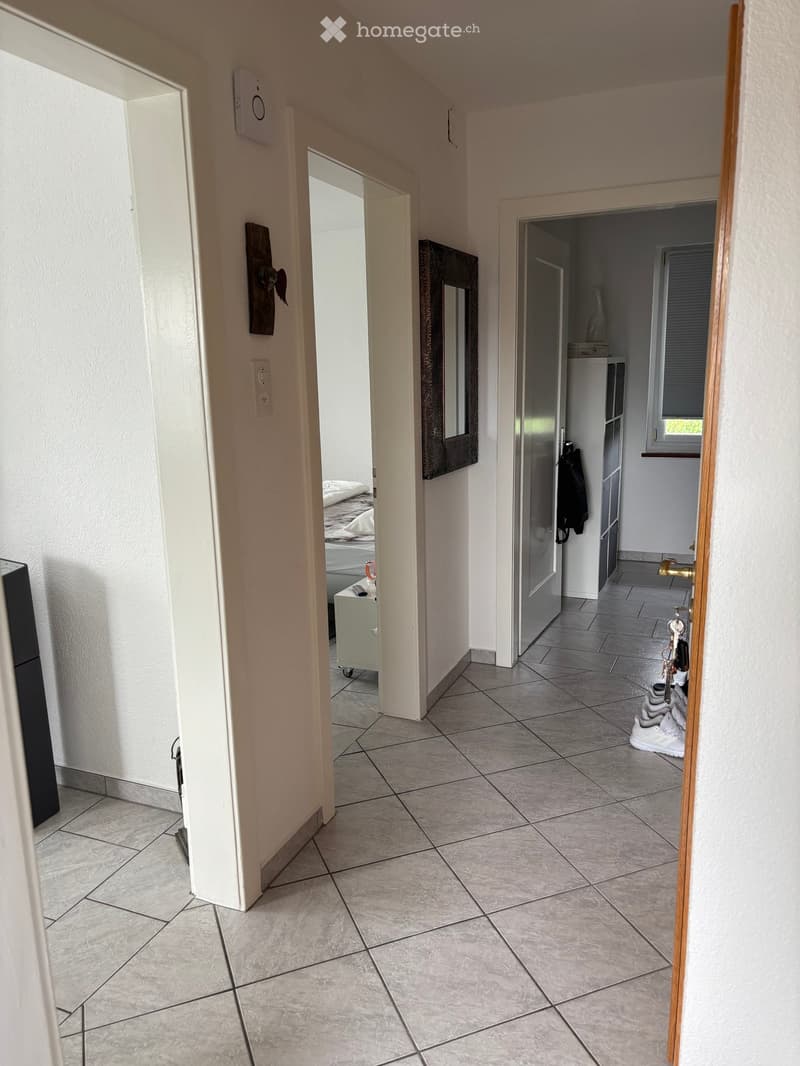 Hallway with tiled floor, open doors leading to bedroom and closet, visible shoes and a mirror in the adjacent rooms.