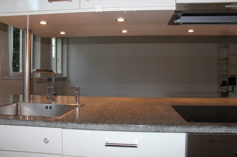Modern kitchen with granite countertops, stainless steel sink and faucet, induction cooktop, white cabinets, and a range hood.