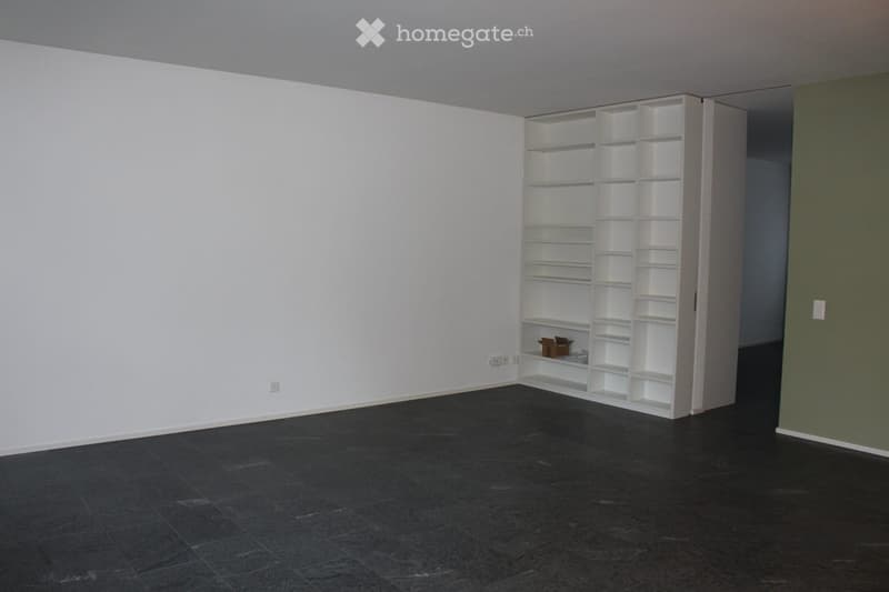 Empty room with white walls, dark tiled floor, and a white shelving unit with empty compartments.