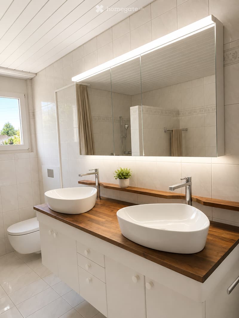 Modern bathroom with two white sinks on a wooden countertop, a large mirror with built-in lighting, a toilet, and a small potted plant on the counter.