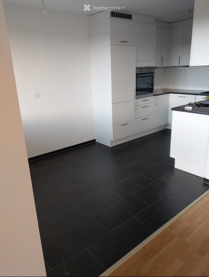 Modern kitchen with white cabinets, black tiled floor, and a built-in oven. The countertop is visible with a few items on it.