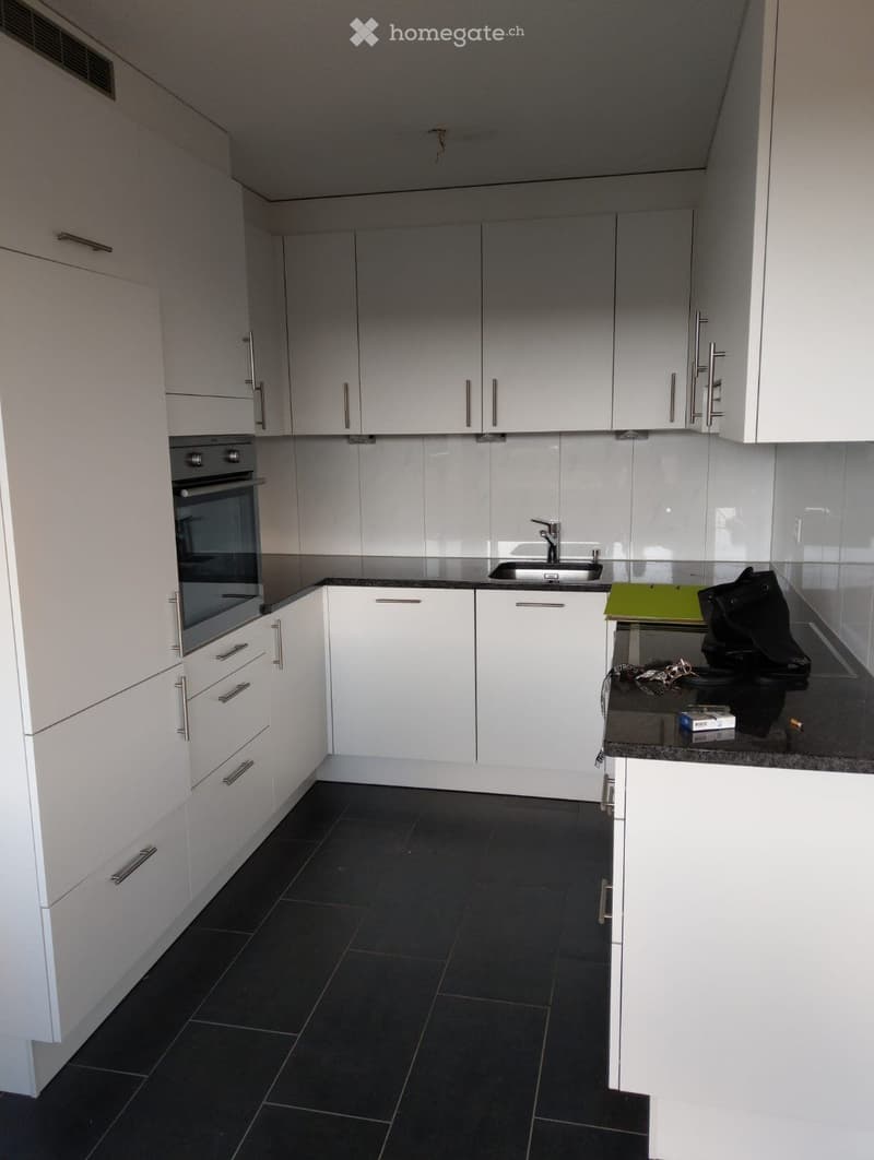 Modern kitchen with white cabinets, stainless steel handles, dark tiled floor, and a stainless steel oven and sink.