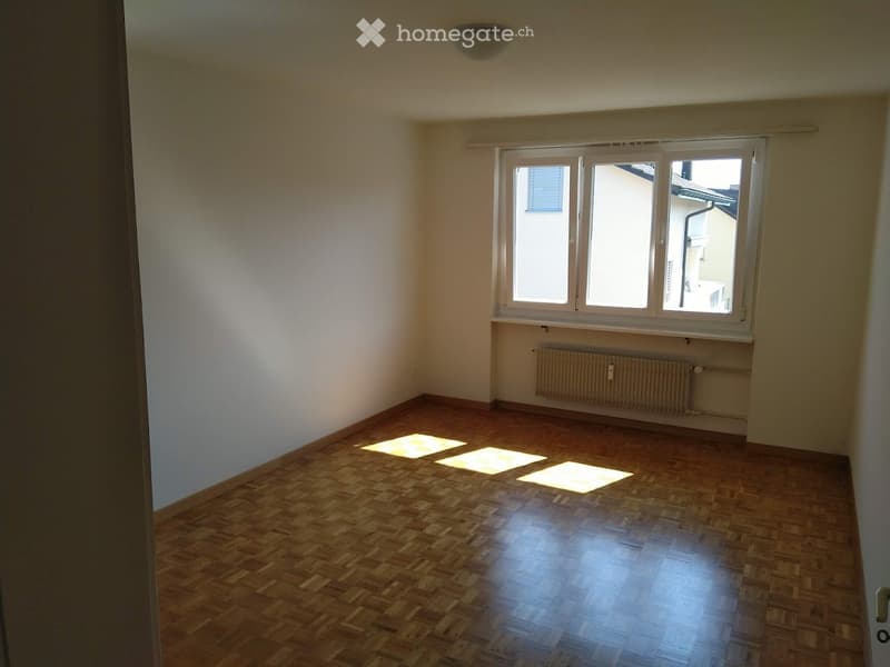 Empty room with wooden flooring, white walls, and a large window letting in natural light. No furniture or equipment is present.