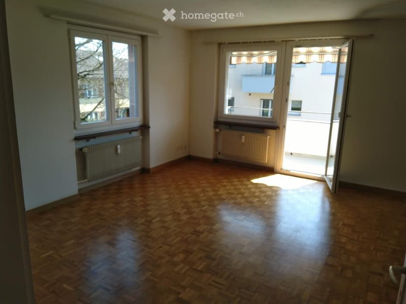 Empty room with wooden flooring, large windows, and radiators. No furniture or equipment present.