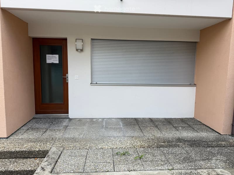 Entrance to a building with a wooden door, a closed metal shutter, and a light fixture above the door.